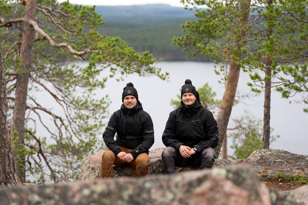 Erkka and Esa sitting on a rock on a forested hill, with a lake below them.
