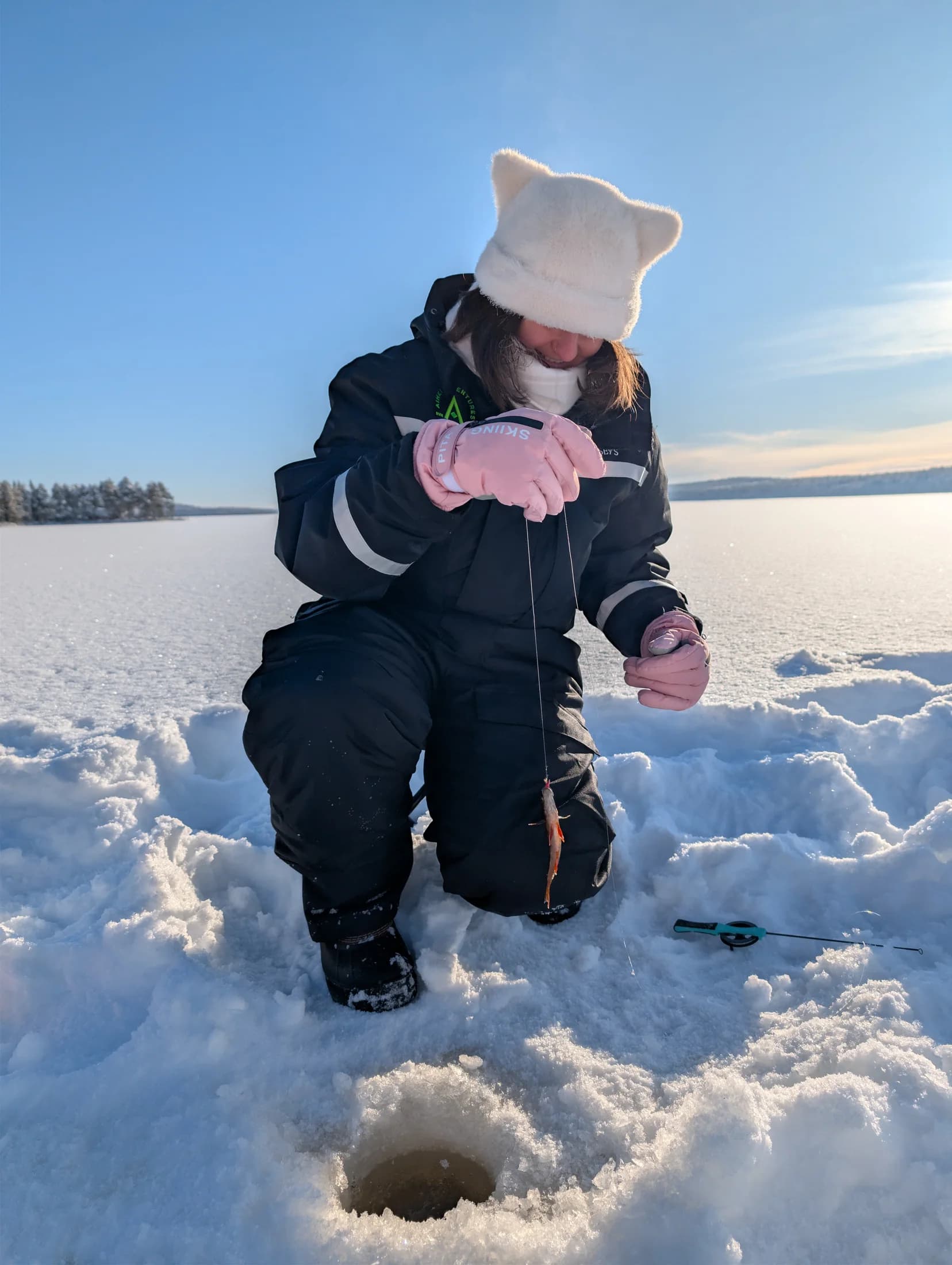 A guest checking a fishing line beside a hole in the ice